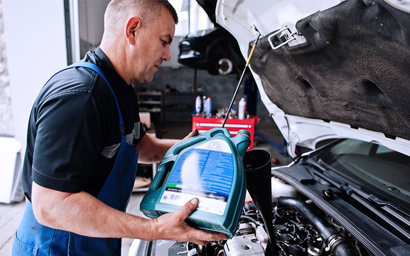 Mecânico reabastece fluído lubrificante do motor de um veículo.